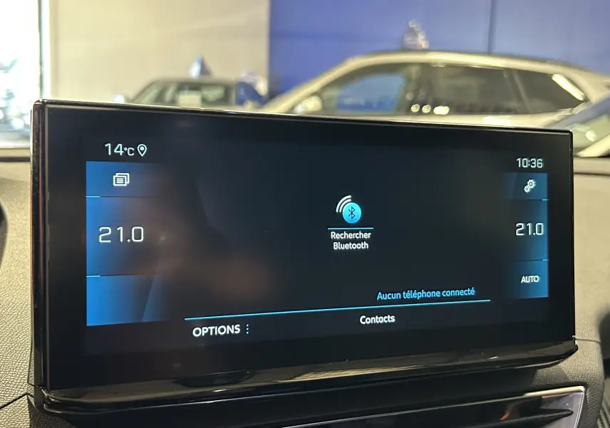 Écran tactile central du Peugeot 5008 2024 affichant la recherche Bluetooth, avec tableau de bord et vitre arrière flous en arrière-plan.