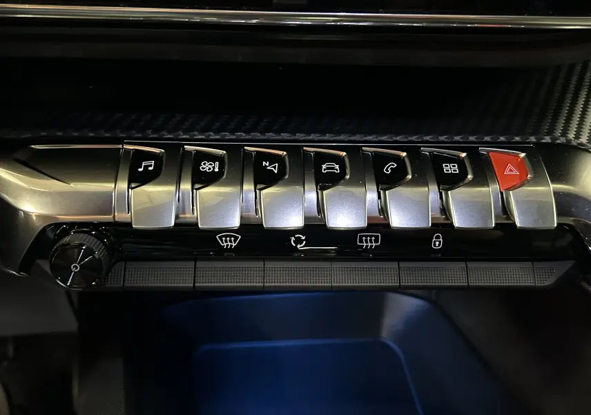 Gros plan sur la rangée de boutons métalliques et rouge d'alerte du tableau de bord du Peugeot 5008 Gris Platinium 2024.