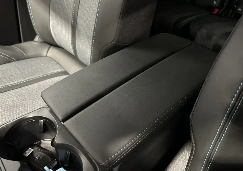 Accoudoir central noir avec surpiqûres bleues entre les sièges avant du Peugeot 5008 Gris Platinium 2024.