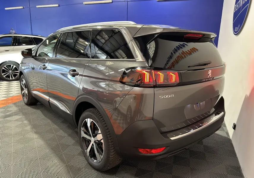 Peugeot 5008 gris Platinium vue 3/4 arrière droit, avec feux arrière allumés et jantes alliage bicolores.