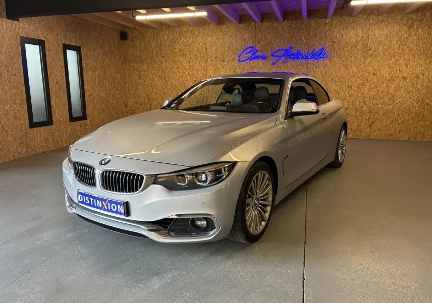 BMW Série 4 Cabriolet gris vue 3/4 avant droit dans un showroom avec éclairage intérieur et logo néon bleu.