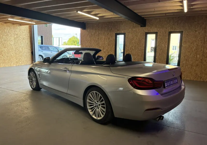 BMW Série 4 Cabriolet gris vue 3/4 arrière droit, capote ouverte, dans un garage lumineux avec murs en bois.