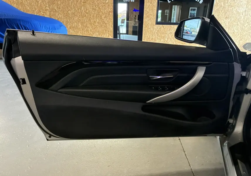 Intérieur côté gauche de la porte ouverte d'une BMW Série 4 Cabriolet gris, avec garniture noire et poignée argentée.