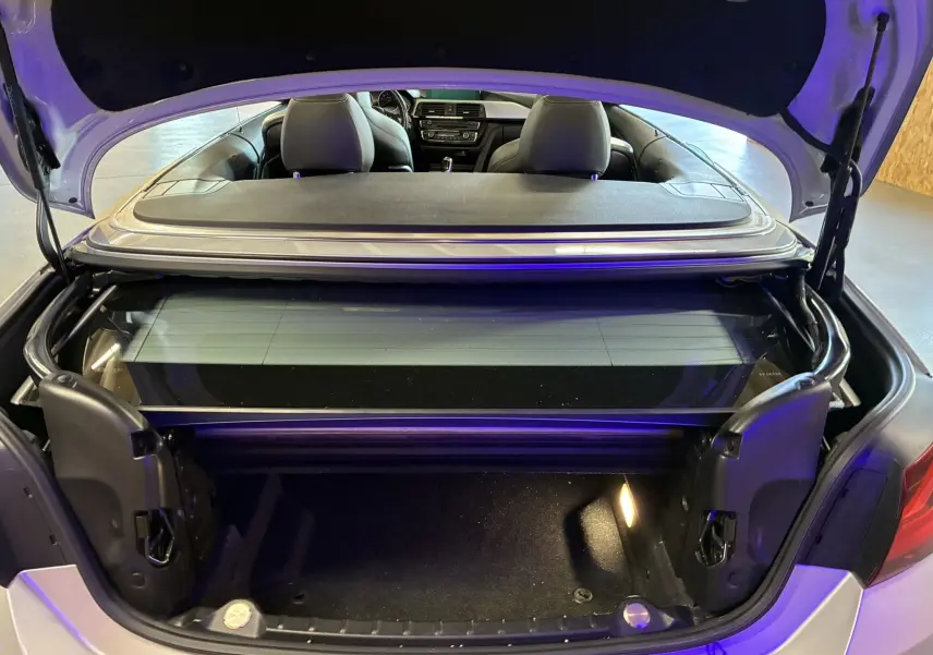 Vue arrière du coffre ouvert d'une BMW Série 4 Cabriolet gris, montrant l'intérieur et les sièges noirs.