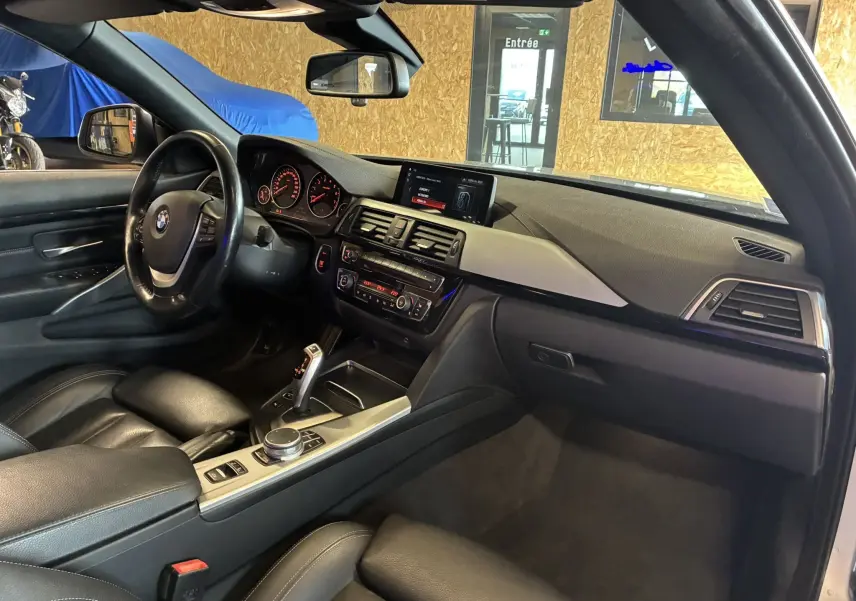 Vue intérieure côté conducteur d'une BMW Série 4 Cabriolet gris, avec tableau de bord noir et écran central lumineux.
