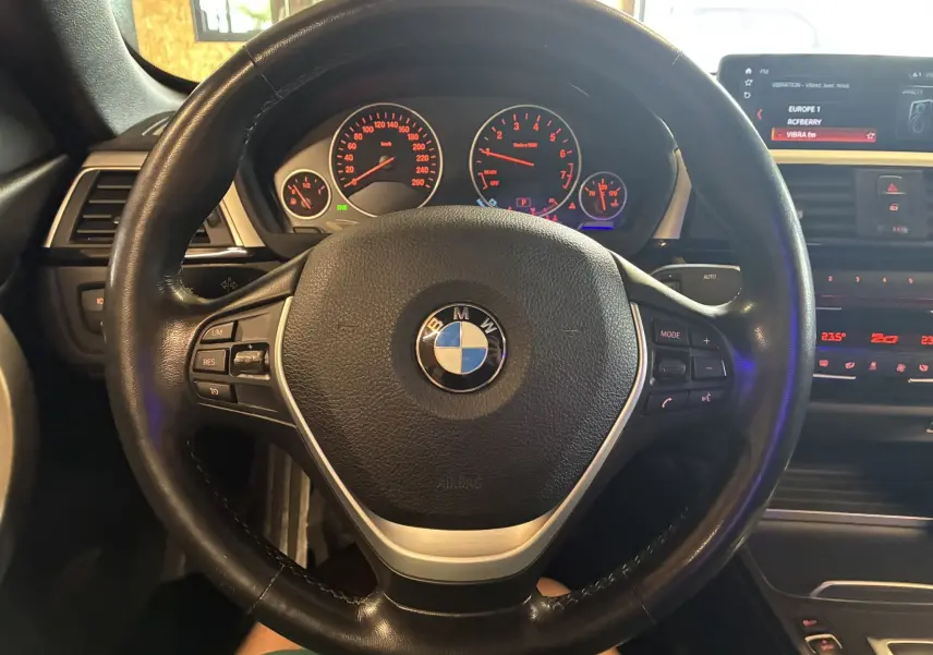 Vue rapprochée du volant en cuir noir d'une BMW Série 4 Cabriolet F33 420i 2019 avec tableau de bord et écran multimédia allumés.