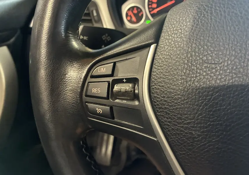 Gros plan sur la partie gauche du volant en cuir noir de la BMW Série 4 Cabriolet gris, avec commandes intégrées.