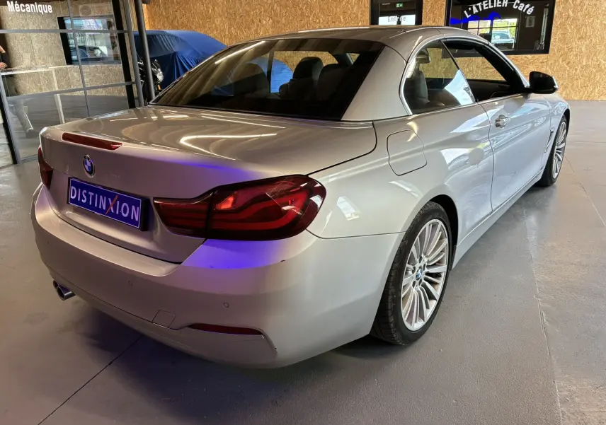 BMW Série 4 Cabriolet gris vue 3/4 arrière droit, toit rigide fermé, jantes multi-branches en intérieur d'atelier.