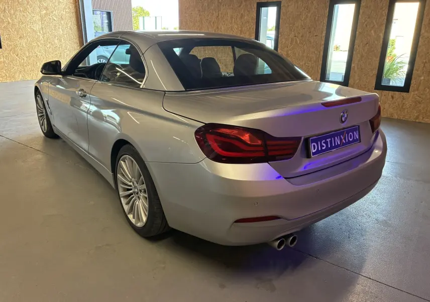 BMW Série 4 Cabriolet gris vue 3/4 arrière droit, toit rigide fermé, double sortie d’échappement visible en intérieur lumineux.