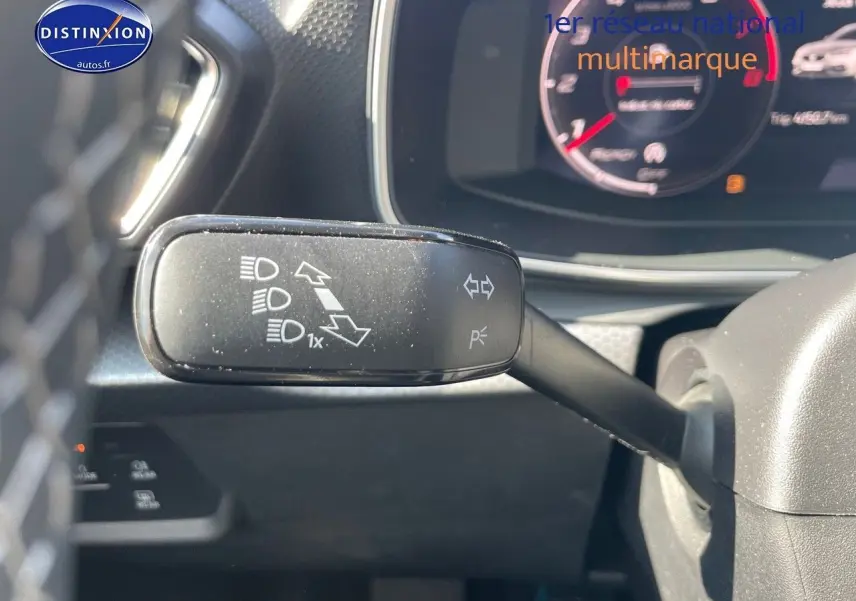 Gros plan sur la manette de clignotant à gauche du volant du SEAT LEON gris métallique, tableau de bord numérique en arrière-plan.