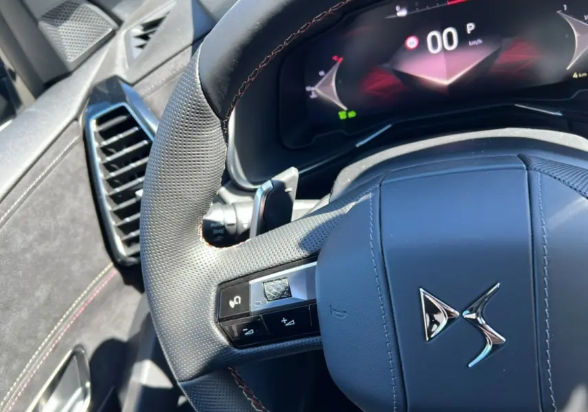 Gros plan sur le volant en cuir perforé du DS7 2025 gris titane, avec commandes intégrées et tableau de bord numérique.