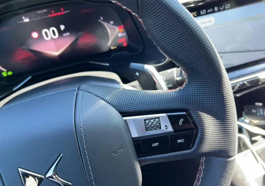 Gros plan sur le volant perforé et les commandes du DS7 2025, avec tableau de bord numérique en arrière-plan.