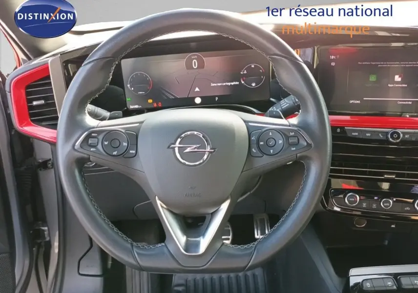 Vue rapprochée du volant Opel Mokka GS Line 2022 avec tableau de bord numérique et inserts rouges autour de la console centrale.
