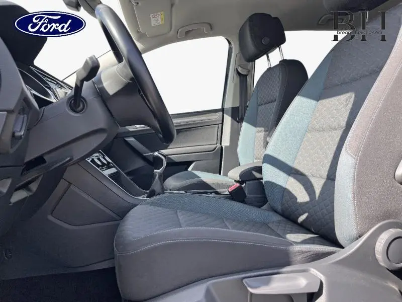 Vue intérieure côté conducteur du Volkswagen Touran 2020, sièges tissu noir et bleu avec accoudoir central.