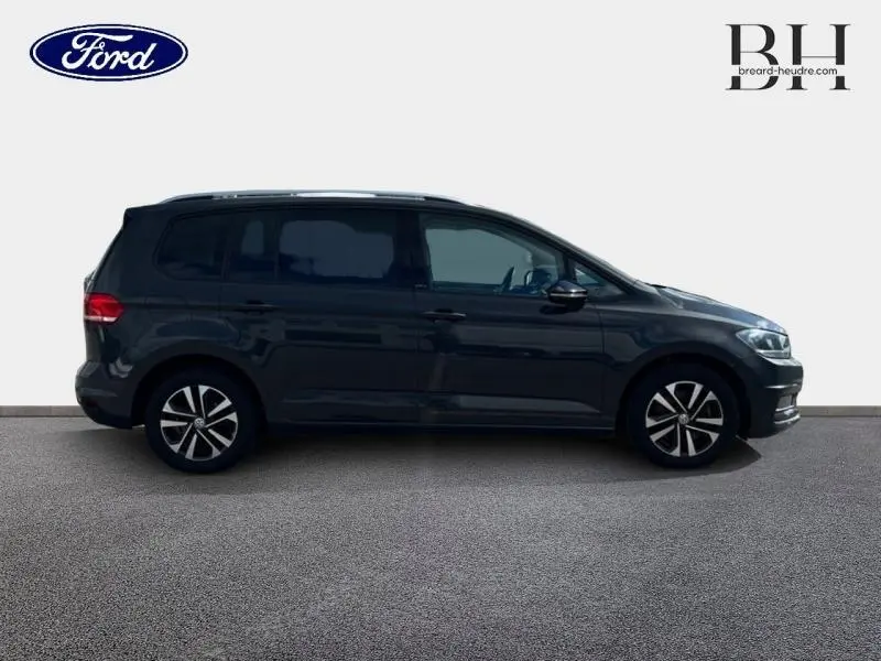 Vue de profil côté gauche d'un Volkswagen Touran gris Urano 7 places, avec vitres arrière teintées et jantes alliage.
