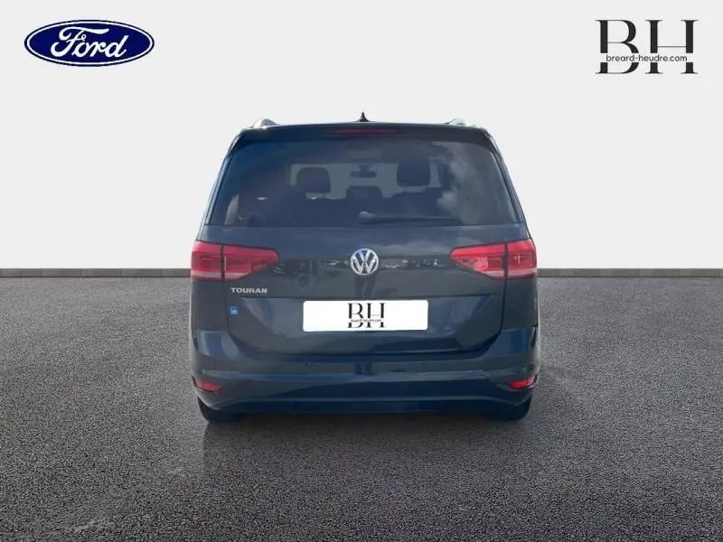 Vue arrière d'un Volkswagen Touran gris Urano avec feux rouges et logo VW bien visibles.