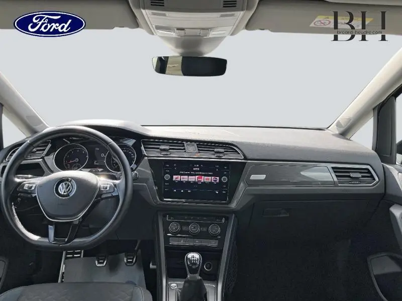Vue intérieure avant du Volkswagen Touran gris Urano 2020, tableau de bord avec écran tactile et volant multifonction.