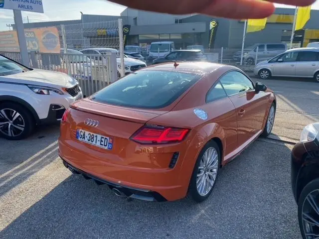 Audi TT 40 TFSI orange vue 3/4 arrière droit, avec jantes argentées et feux arrière LED allumés.