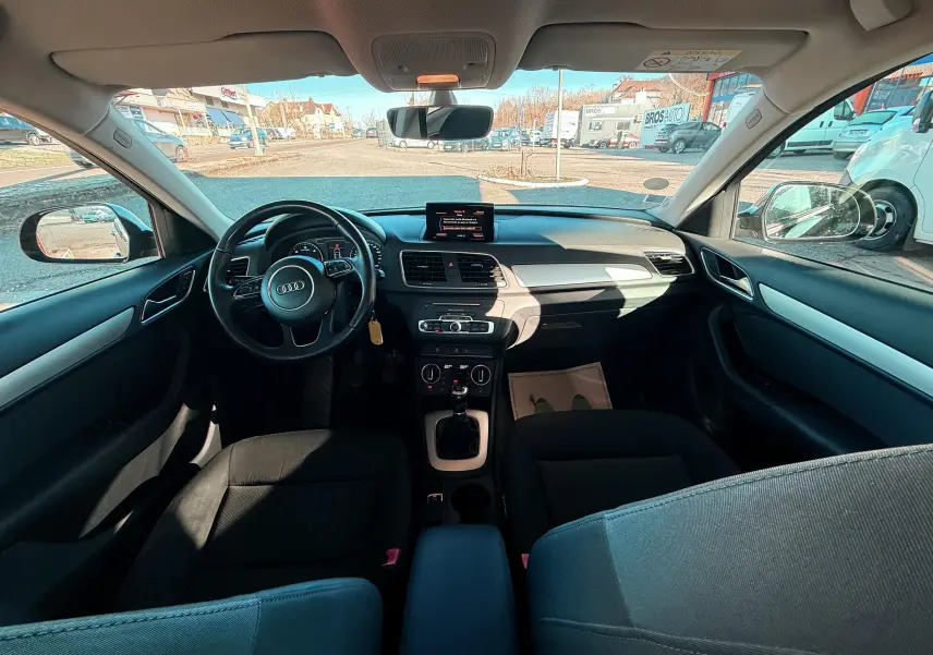 Vue intérieure avant de l'Audi Q3 noire 2016, montrant le tableau de bord, le volant et la console centrale avec boîte manuelle.