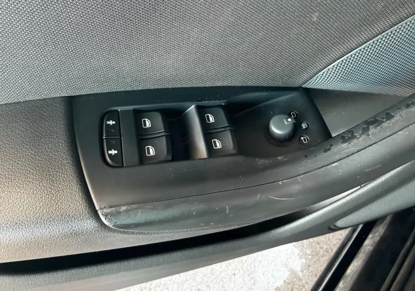Gros plan sur les commandes de lève-vitres et réglage des rétroviseurs côté conducteur d’un Audi Q3 noir de 2016.