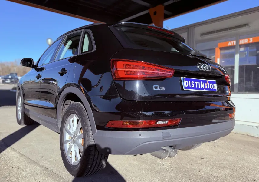 Vue 3/4 arrière droite d’un Audi Q3 noir 2016 avec feux arrière allumés et double sortie d’échappement visible.