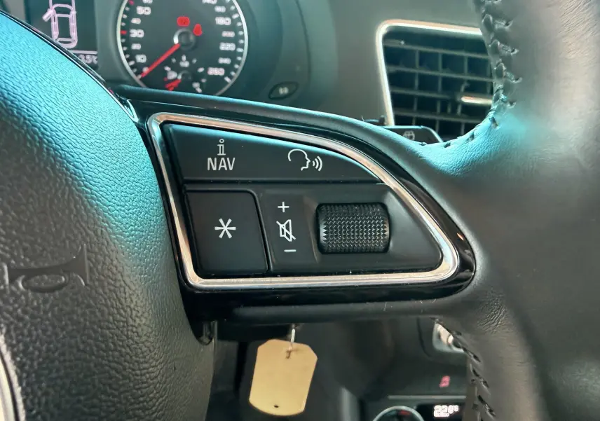 Gros plan sur les commandes gauche du volant en cuir noir de l'Audi Q3 2016, avec tableau de bord en arrière-plan.