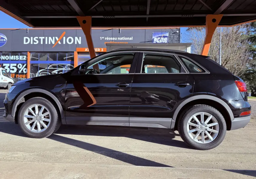 Audi Q3 noir vue de profil côté gauche, stationné sous un abri avec jantes alliage visibles.