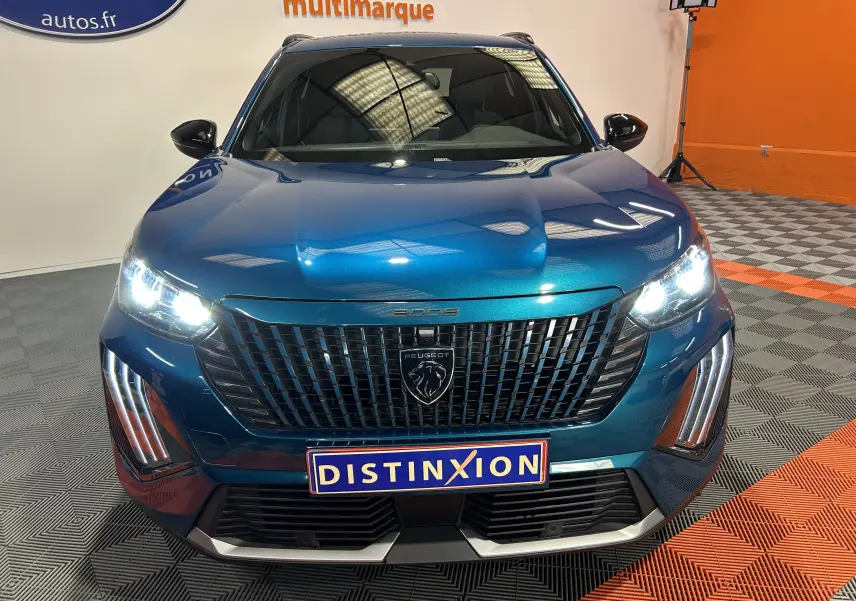 Vue avant d'un Peugeot 2008 bleu Obsession avec phares allumés et calandre noire distinctive en intérieur showroom.