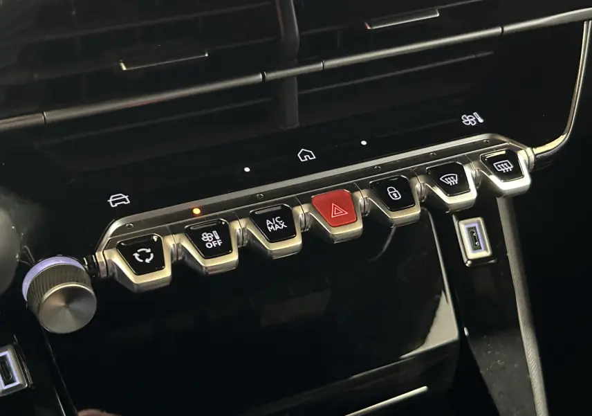 Gros plan sur la rangée de commandes métalliques du tableau de bord du Peugeot 2008 II Ph.2 Allure Hybrid 145, finition noire.