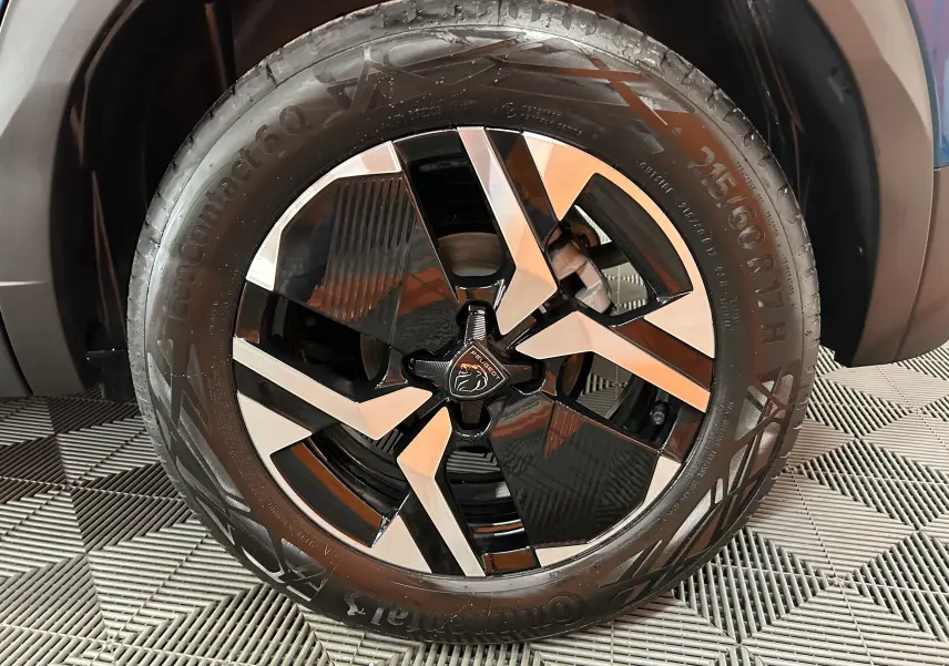 Gros plan sur la jante avant droite noire et argentée du Peugeot 2008 Bleu Obsession 2025 hybride sur tapis texturé.
