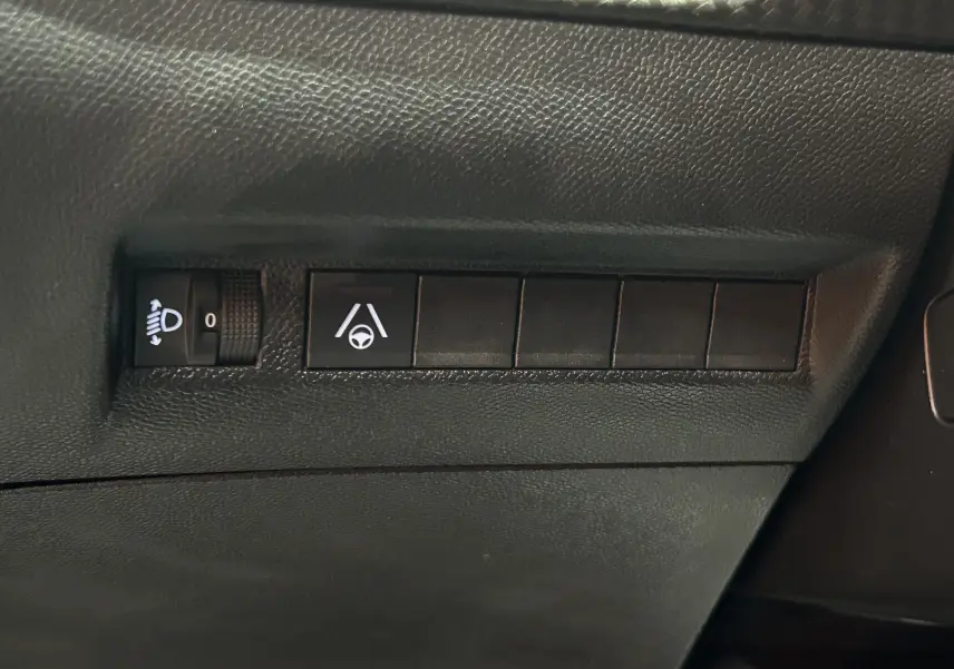 Gros plan sur les commandes d'assistance à la conduite et réglage des phares dans l'habitacle du Peugeot 2008 Bleu Obsession.