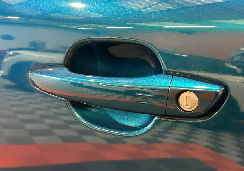 Gros plan sur la poignée de porte côté gauche en Bleu Obsession métallisé du Peugeot 2008 II Ph.2 Allure Hybrid 145.