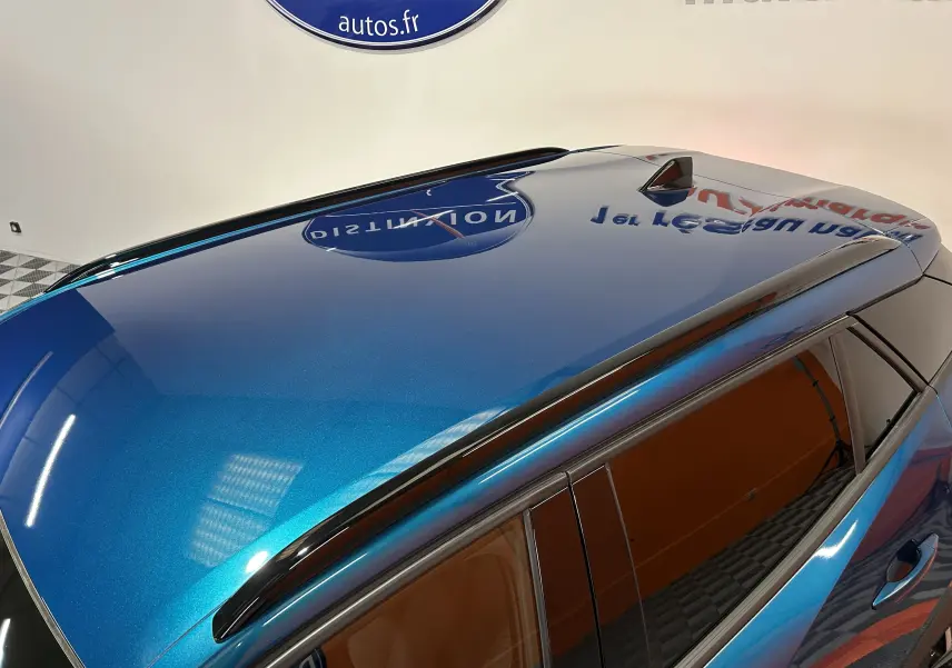 Vue plongeante sur le toit bleu métallisé du Peugeot 2008 II Ph.2 Allure Hybrid avec antenne requin et barres de toit noires.