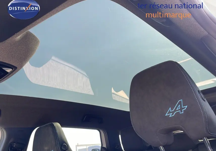 Détail du ciel de toit panoramique et appuie-tête noir avec logo Alpine bleu dans un Renault Espace blanc nacré.