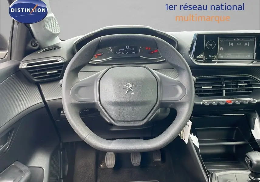 Vue frontale du poste de conduite de la Peugeot 208 blanche, volant compact et tableau de bord numérique visible.