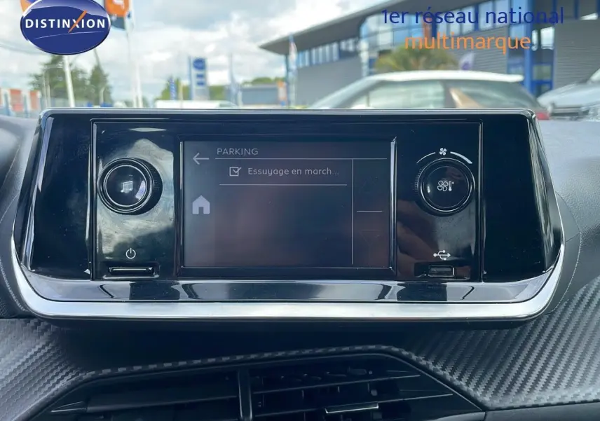 Écran tactile central du tableau de bord d'une Peugeot 208 blanc banquise, avec commandes de climatisation visibles.