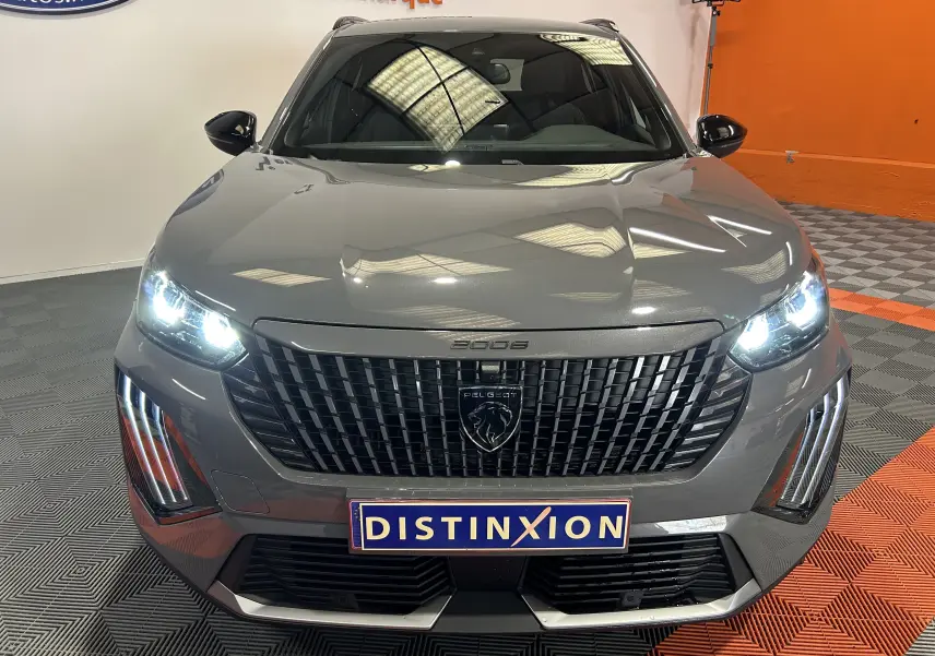 Vue avant d’un Peugeot 2008 gris Selenium avec phares allumés et calandre noire distinctive en intérieur showroom.