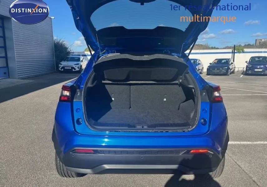 Vue arrière du Nissan Juke 2025 bleu magnétique métal avec coffre ouvert, montrant l’espace de chargement vide.