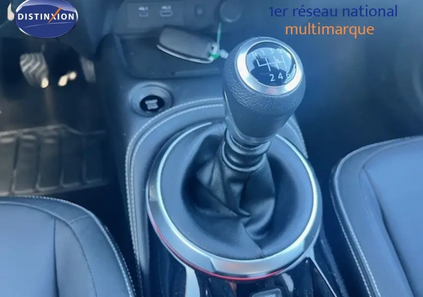 Le levier de vitesse manuel en gros plan dans l'habitacle du Nissan Juke bleu magnétique, avec coutures blanches visibles.