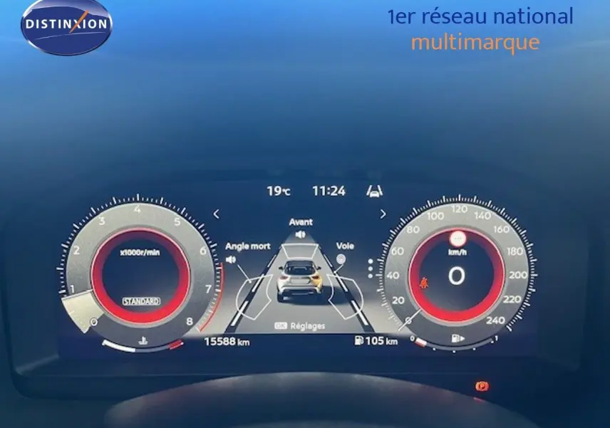 Tableau de bord numérique du Nissan Juke bleu magnétique, affichage central avec alertes d'angle mort et vitesse à zéro.