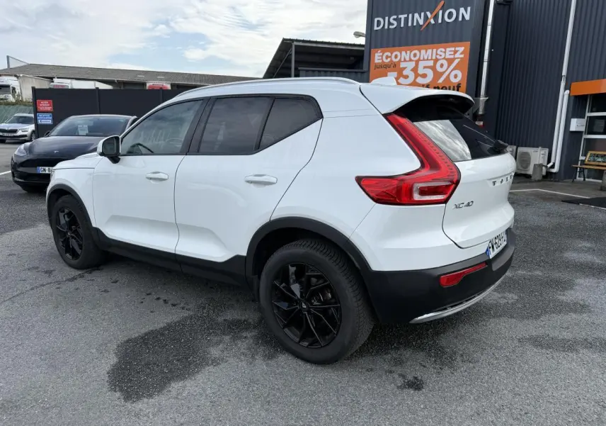 Vue 3/4 arrière droite d'un Volvo XC40 blanc avec jantes alliage noires et protections noires sur passages de roues.