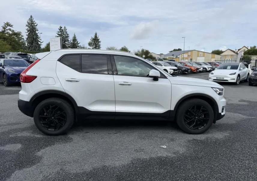 Profil côté gauche d'un Volvo XC40 blanc avec jantes alliage noires 18 pouces sur parking extérieur.