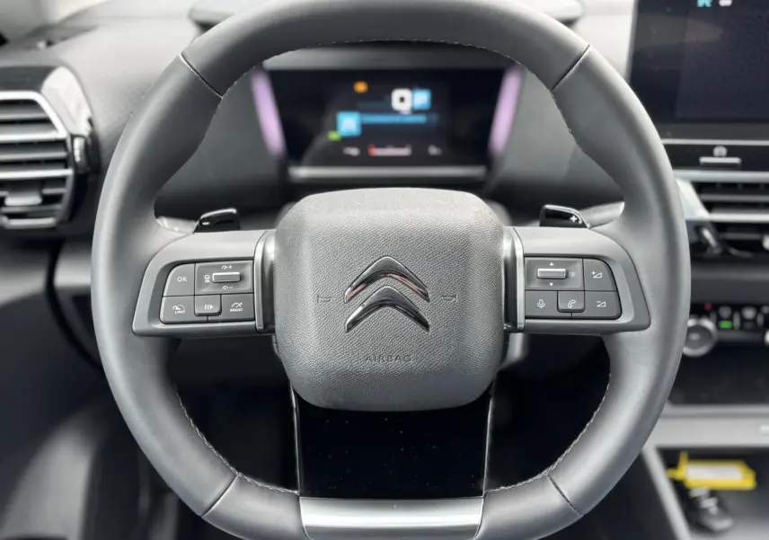 Volant cuir noir avec commandes intégrées du Citroën C4 PureTech 130 2024, intérieur moderne et écran numérique en arrière-plan.