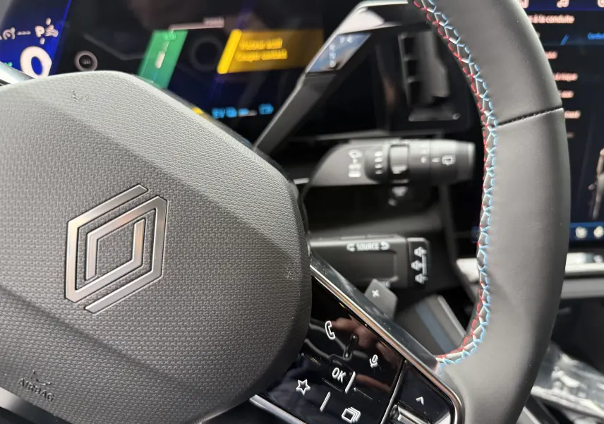Gros plan sur le volant noir avec surpiqûres tricolores du Renault Austral 2025, tableau de bord digital en arrière-plan.