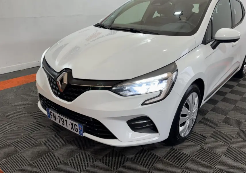 Renault Clio Business TCe 100 blanche vue 3/4 avant droit avec phares LED allumés dans un showroom.