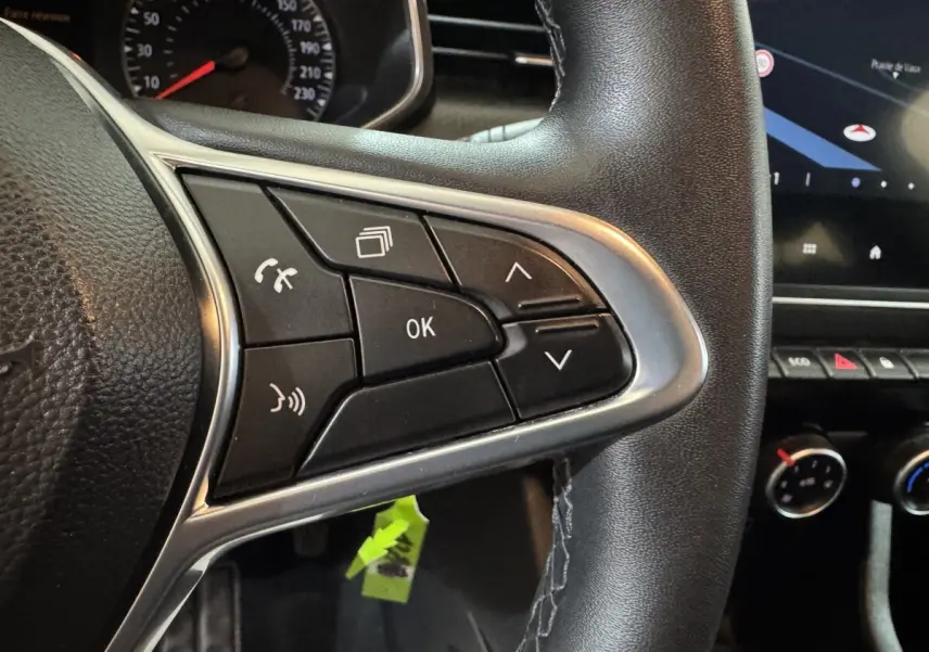 Gros plan sur les commandes multifonctions du volant cuir noir de la Renault Clio Business TCe 100, avec tableau de bord partiel visible.