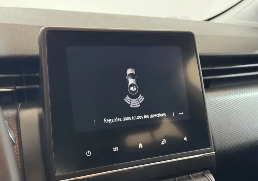 Écran tactile central de la Renault Clio Business blanc, affichant une alerte de détection d'obstacles au stationnement.