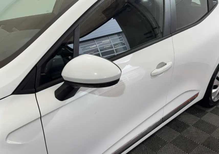 Vue latérale droite rapprochée d'une Renault Clio Business TCe 100 blanche avec rétroviseur blanc et poignée de porte visible.