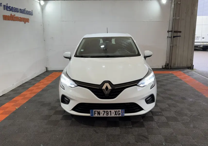 Renault Clio Business TCe 100 blanche vue de face, phares LED allumés dans un garage éclairé.