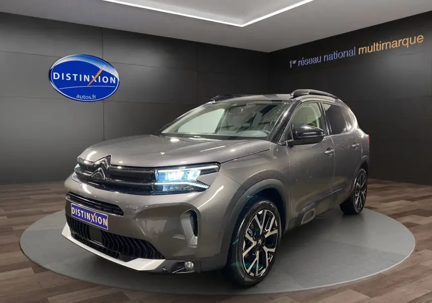 Citroën C5 Aircross gris platinium en 3/4 avant droit avec phares allumés dans un showroom.